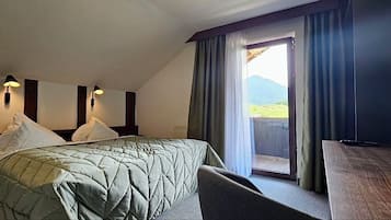 A hotel room with a bed, two bedside lamps, a desk with a chair, a TV, and a balcony with curtains.