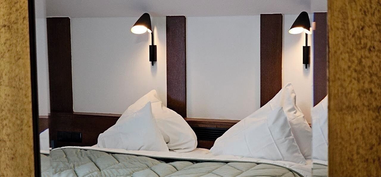 A hotel room with a bed, two wall-mounted lamps, and a wooden headboard.