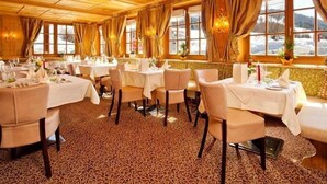 En restaurang med träpanel i tak och på väggarna, bord som är dukade för middag och stora fönster med gardiner.