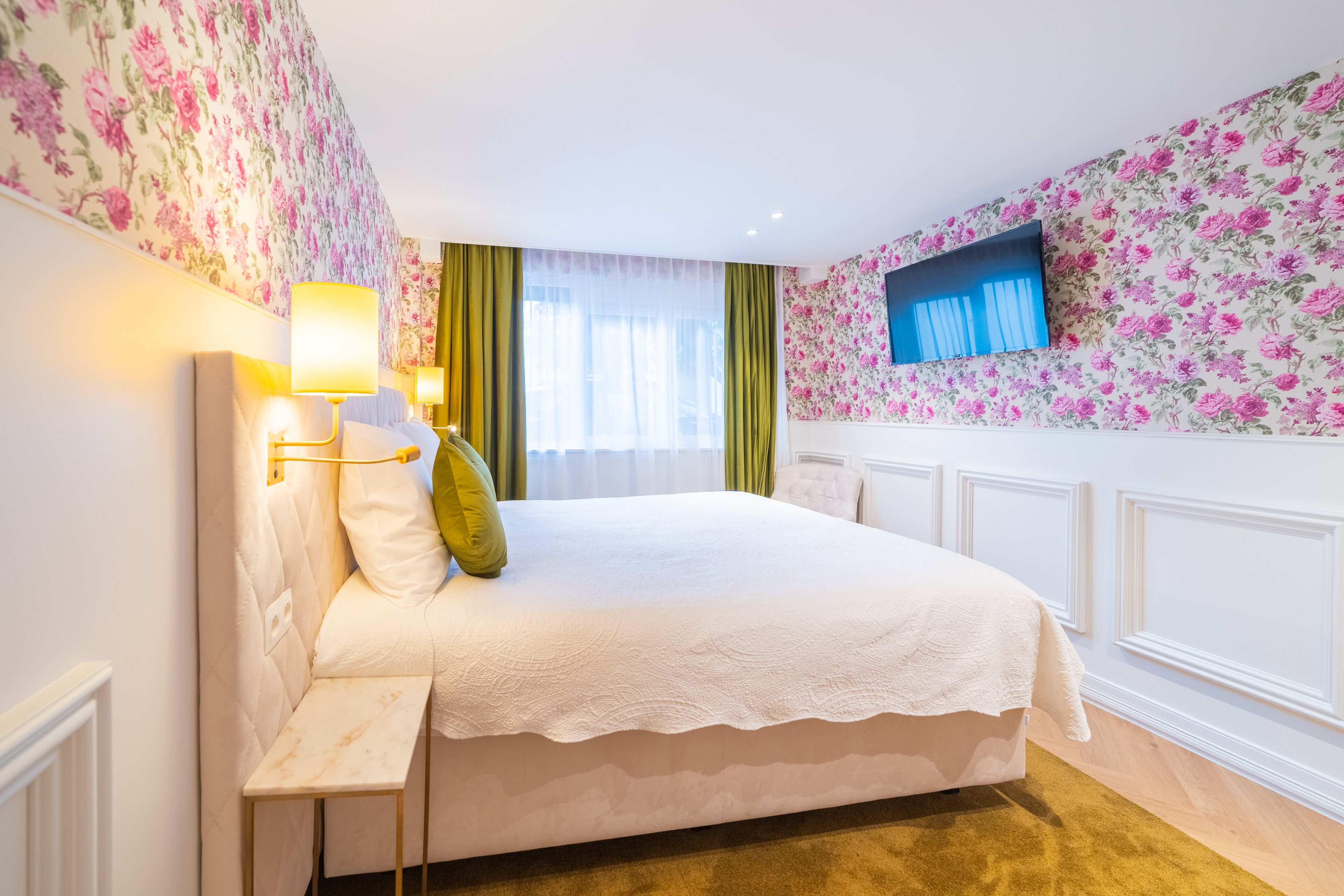 A neatly arranged bedroom with a bed, bedside lamps, and a television on the wall.