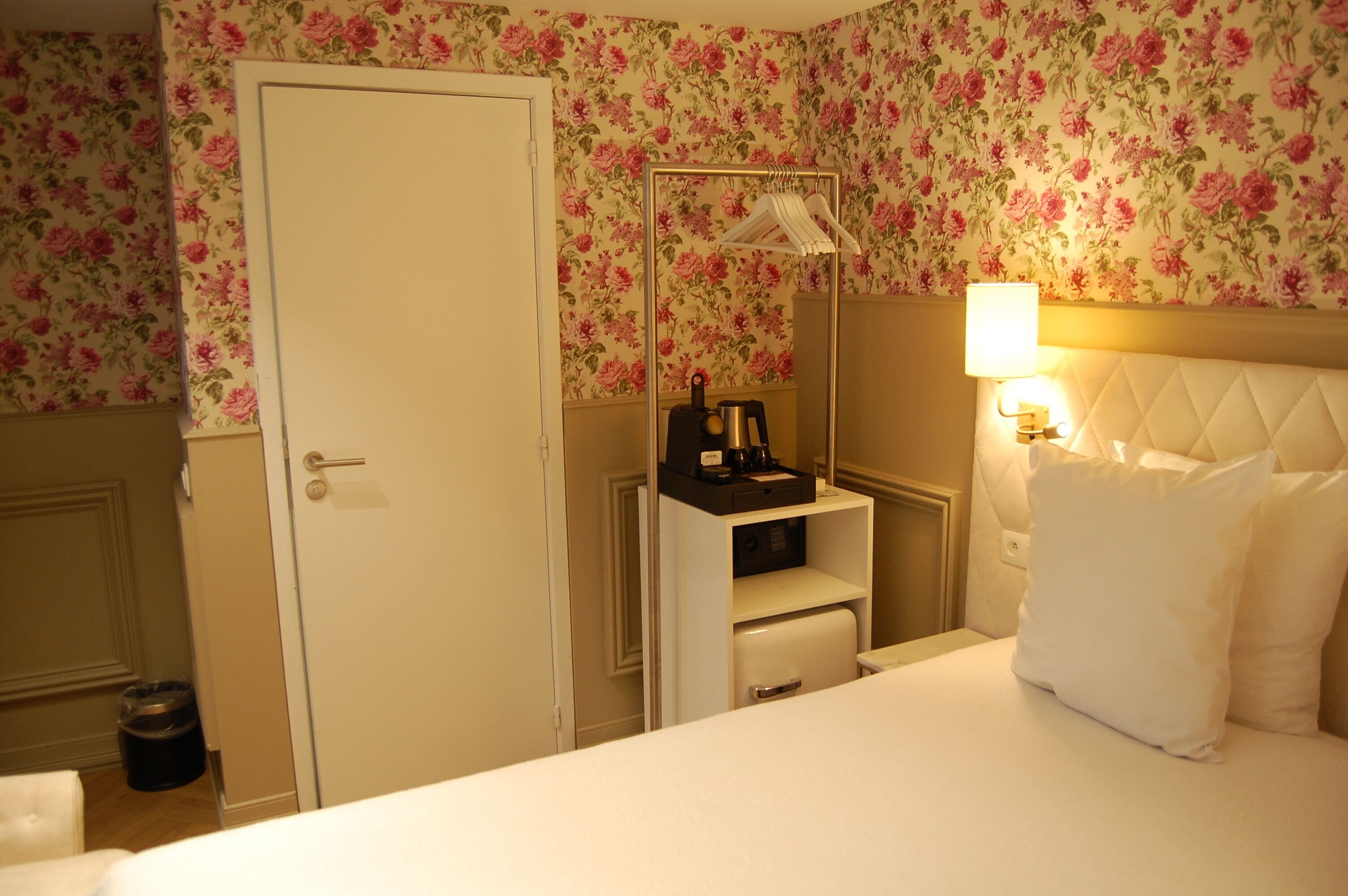 A hotel room with a bed, a dresser, a mirror, a lamp, and floral wallpaper.