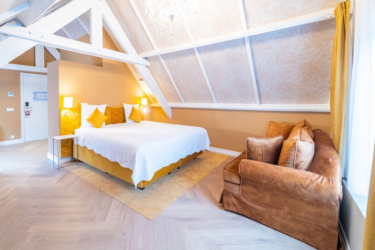 A bedroom with a bed, bedside lamps, a sofa, and a window with curtains.