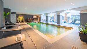 Un área de piscina interior moderna con sillones de descanso y una piscina pequeña.
