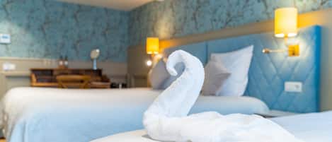 Ett hotellrum med två sängar, en blå sänggavel och en vit handduk formad som en svan på sängen.