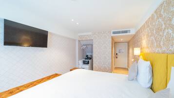 A hotel room with a large bed, a flat-screen TV mounted on the wall, a small kitchenette, and a bathroom visible through an open door.