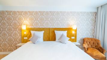 A hotel room with a large bed, two bedside lamps, a tufted headboard, and a brown armchair.