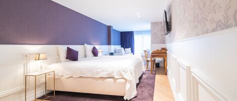 A modern bedroom with a large bed, a bedside table, a desk, and a chair.