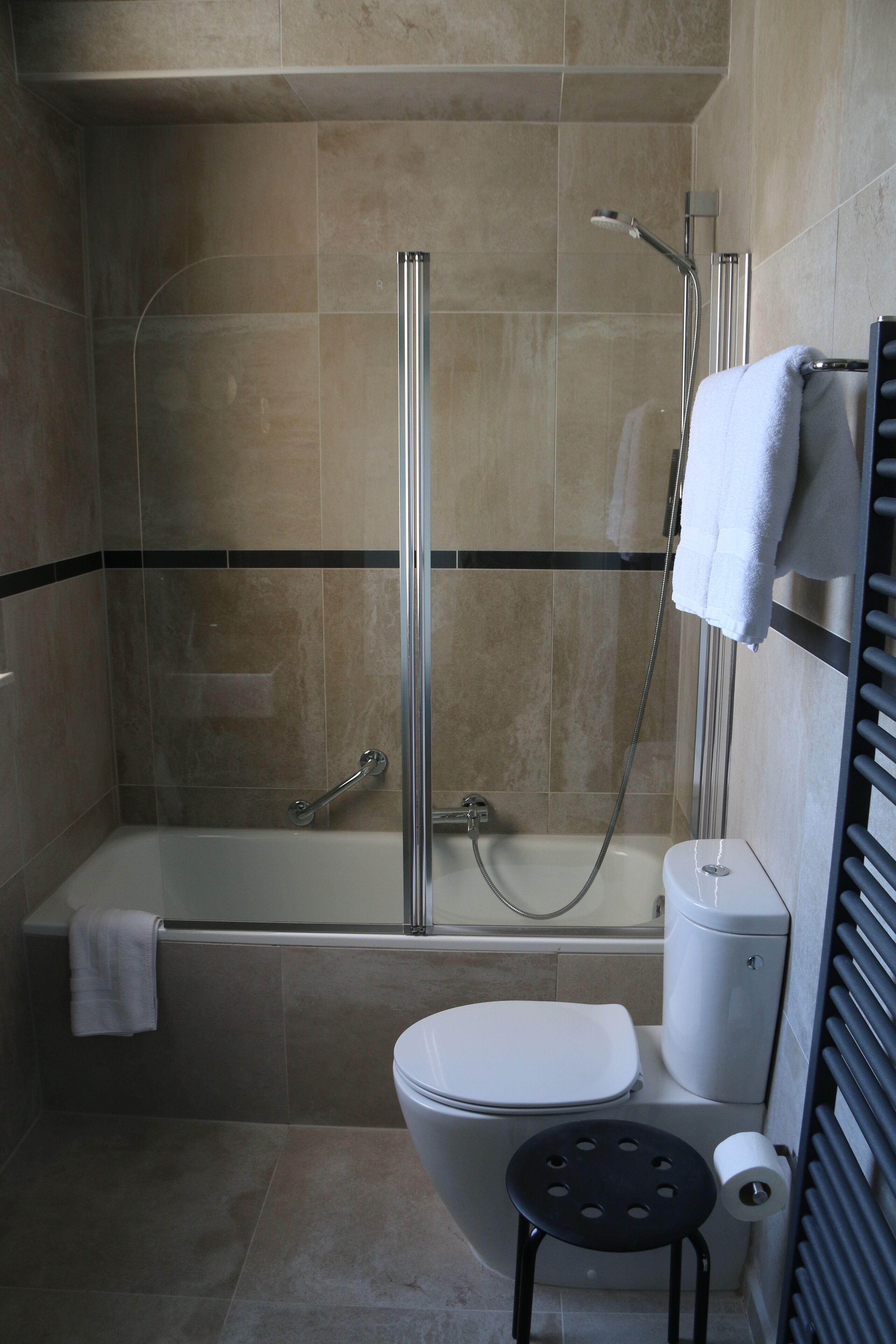 Une salle de bain avec une douche à parois de verre, une baignoire, des toilettes et un petit tabouret.