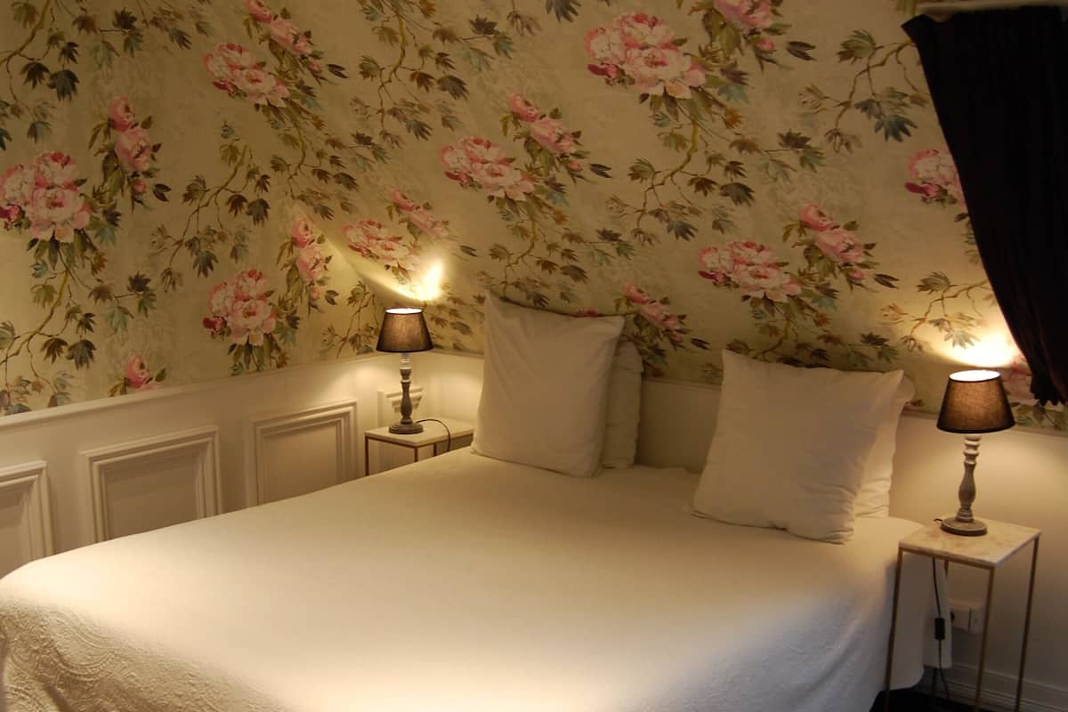 A neatly made bed with a white duvet, two bedside lamps, and a floral wallpaper pattern.