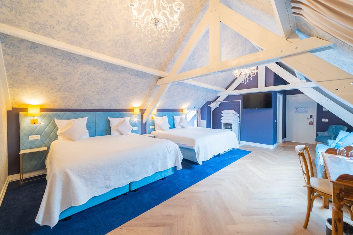 A bedroom with two beds, a chandelier, and a wooden ceiling structure.