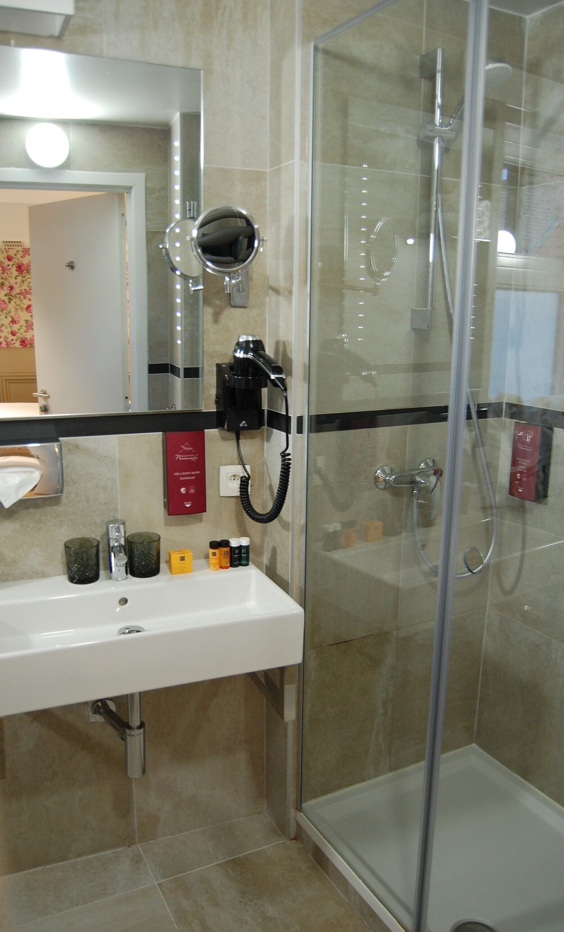 A bathroom with a glass-enclosed shower, a white sink, and a mirror with lights.