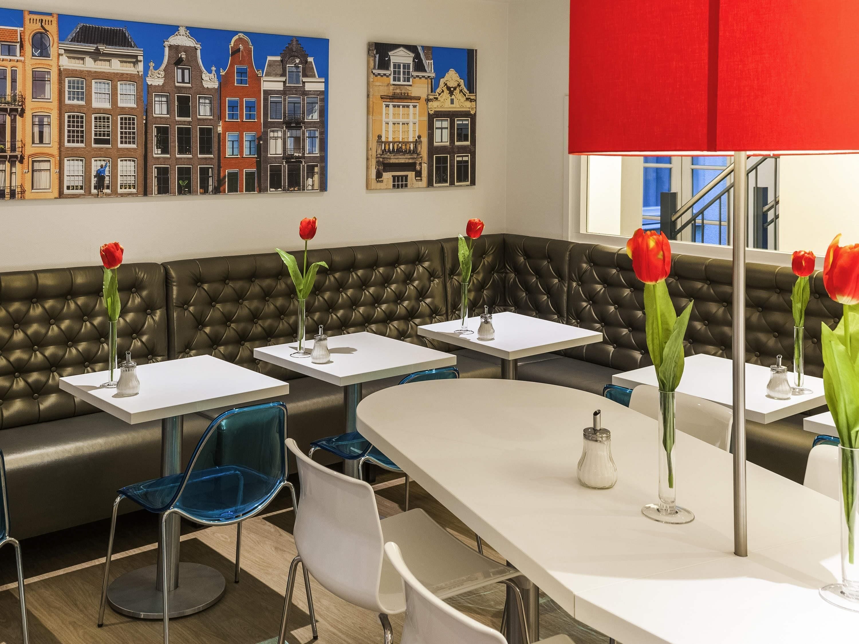 A modern restaurant with a black leather booth seating, white tables, and red tulips in vases.
