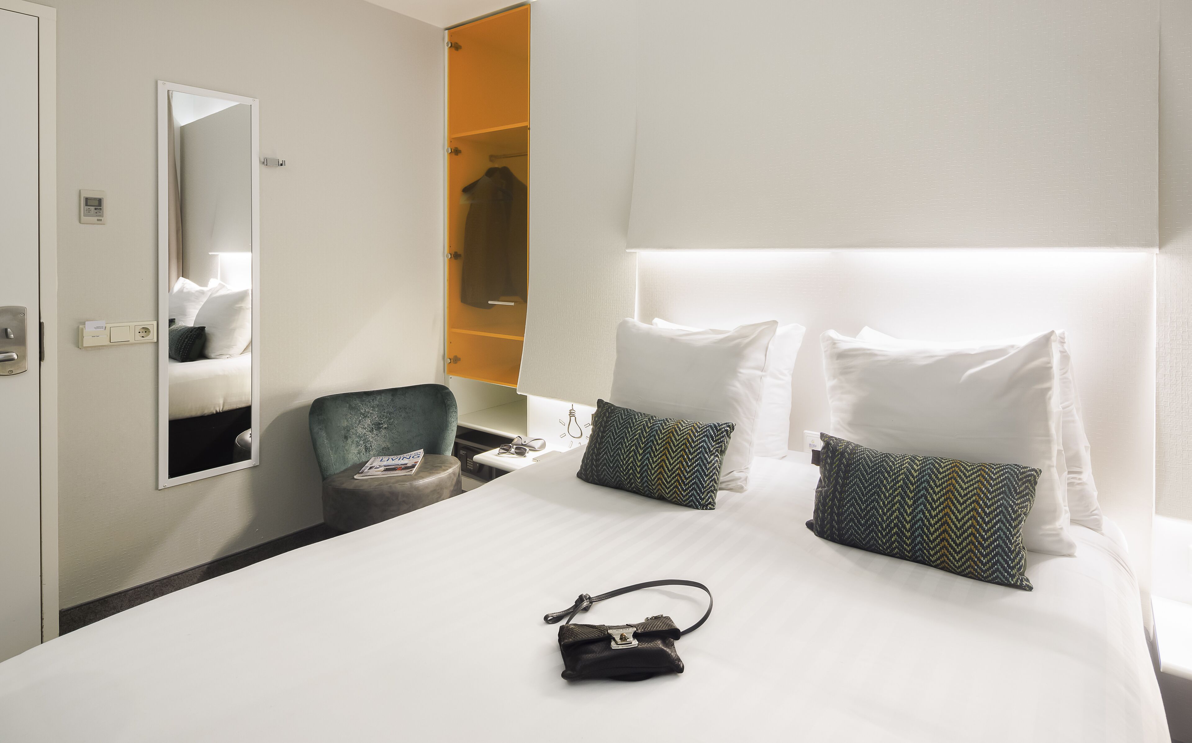A hotel room with a bed, a chair, a mirror, and a wardrobe.