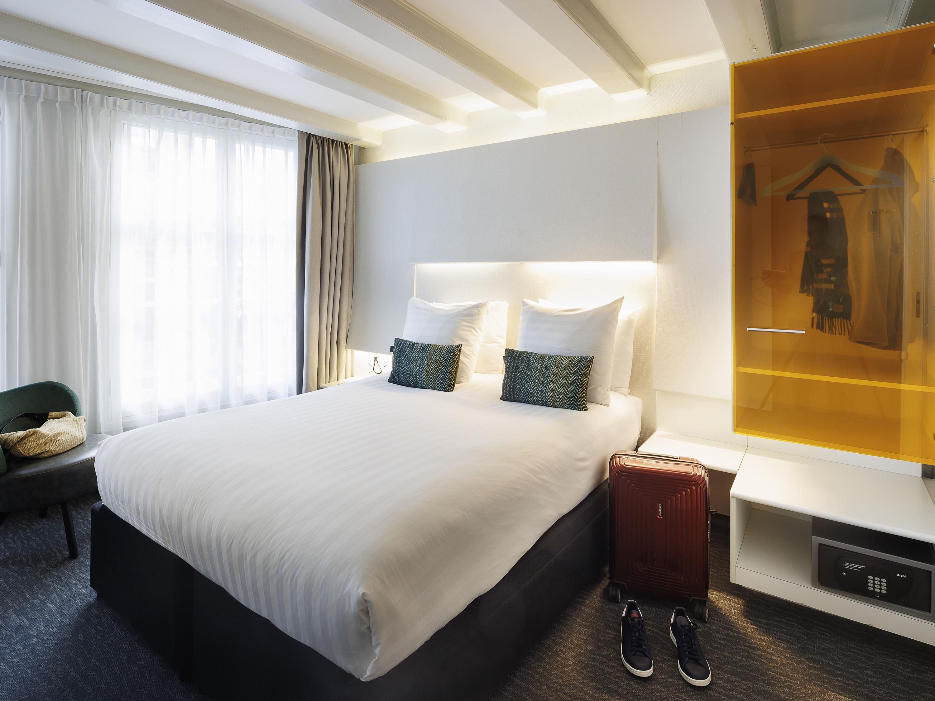 A hotel room with a large bed, a bedside table, a wardrobe, and a chair.