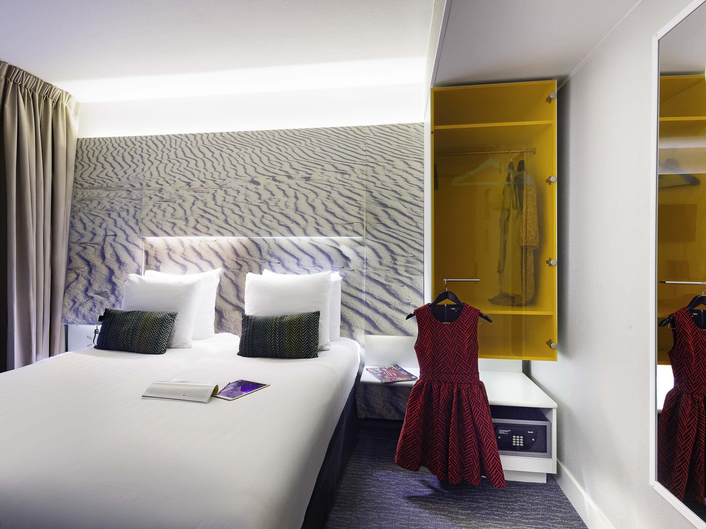 A hotel room with a bed, pillows, a mirror, a wardrobe, and a door.