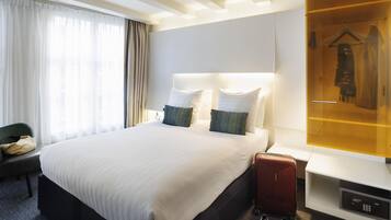 A hotel room with a large bed, a bedside table with a lamp, a wardrobe, and a suitcase on the floor.