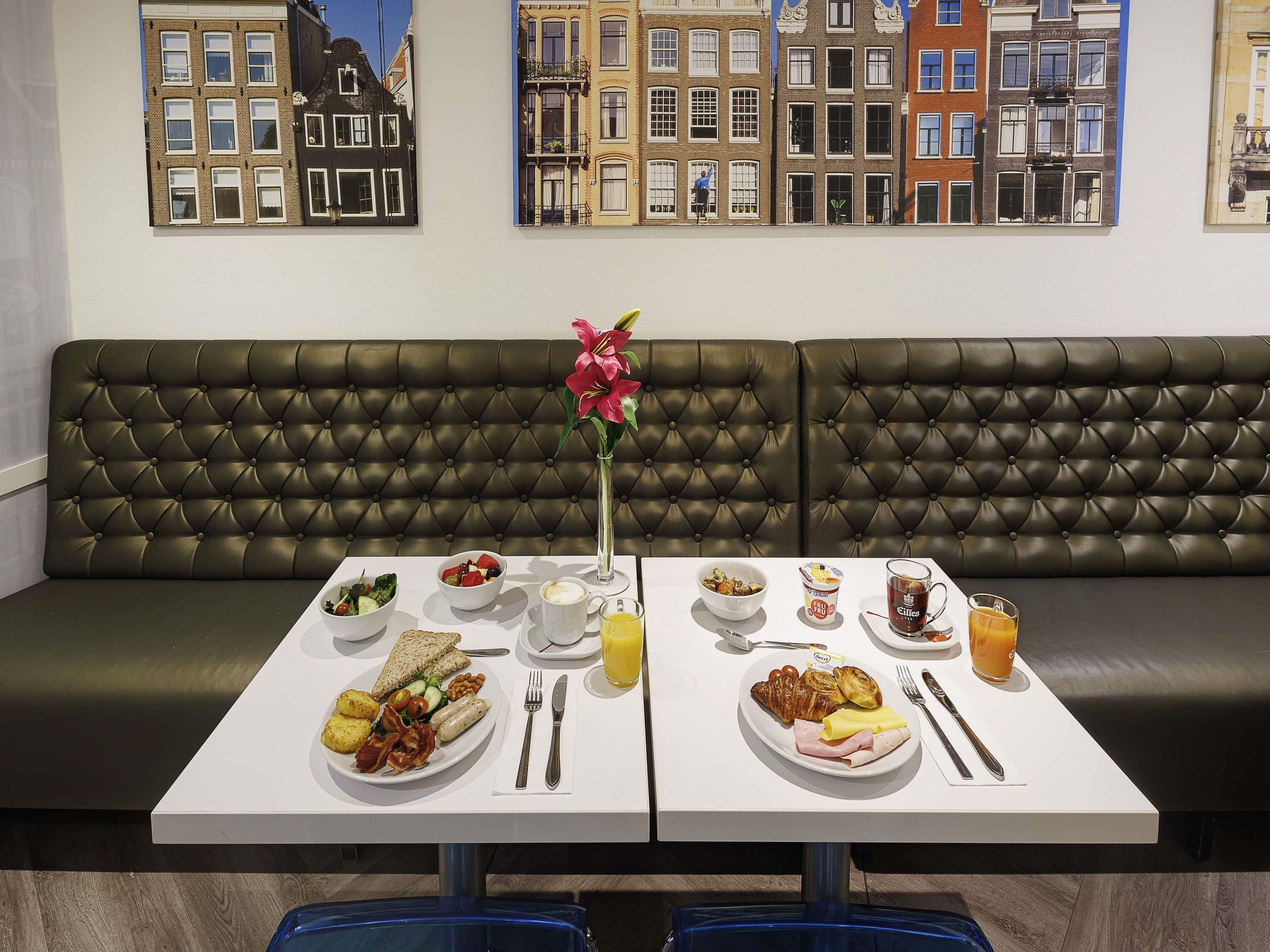 Een eetgedeelte met een bank, twee borden met ontbijt, een vaas met een bloem en een uitzicht op de stad.