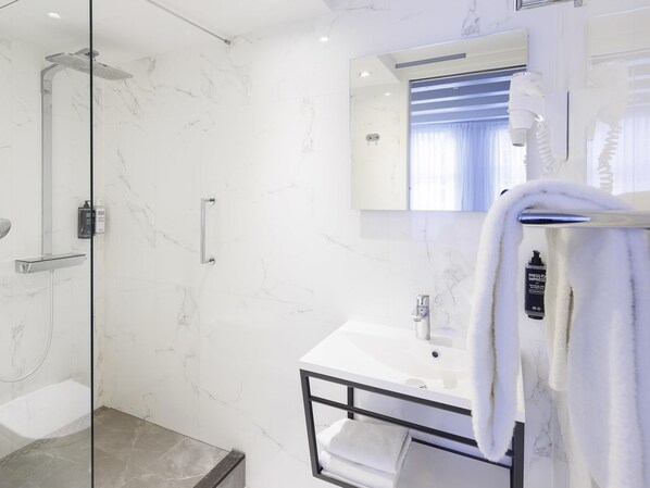 Un baño moderno con ducha de mampara de vidrio, lavamanos blanco y barra para toallas.