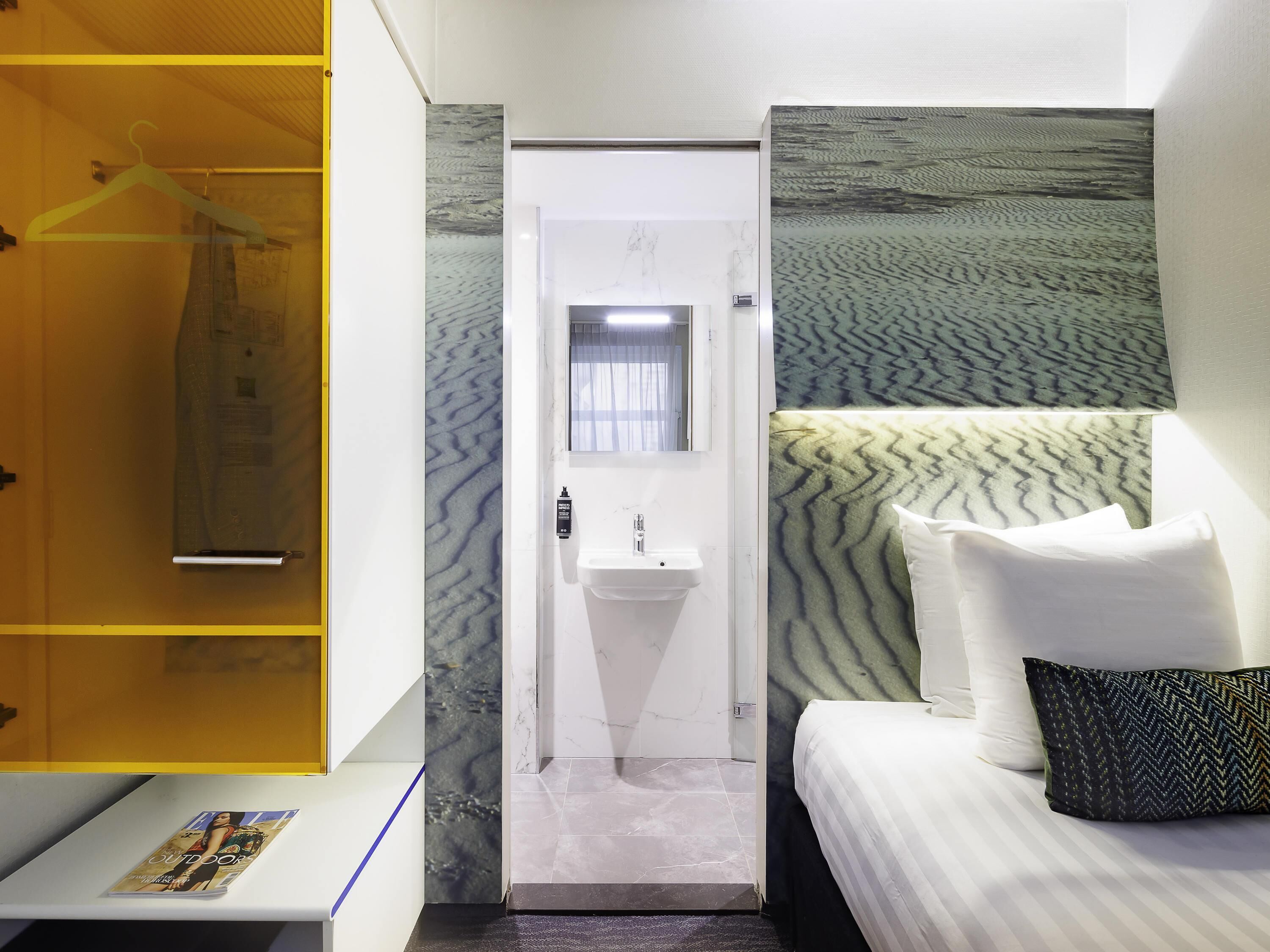 A hotel room with a bed, a bathroom with a sink, and a wardrobe.