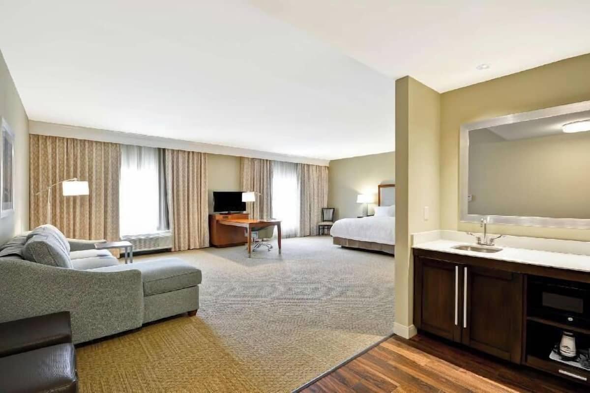 A hotel room with a sofa, a TV, a desk, a bed, a bathroom, and a kitchen area.