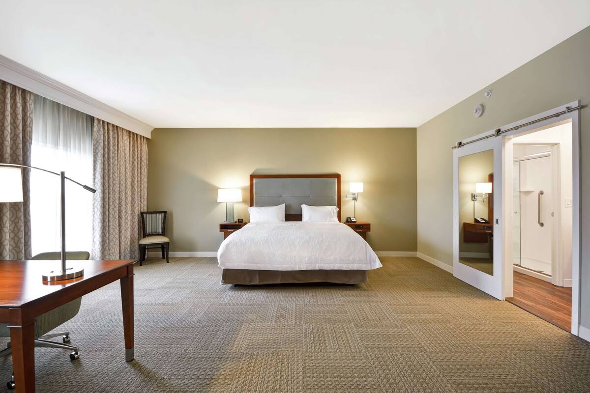 A hotel room with a large bed, bedside lamps, a desk, and a wardrobe.
