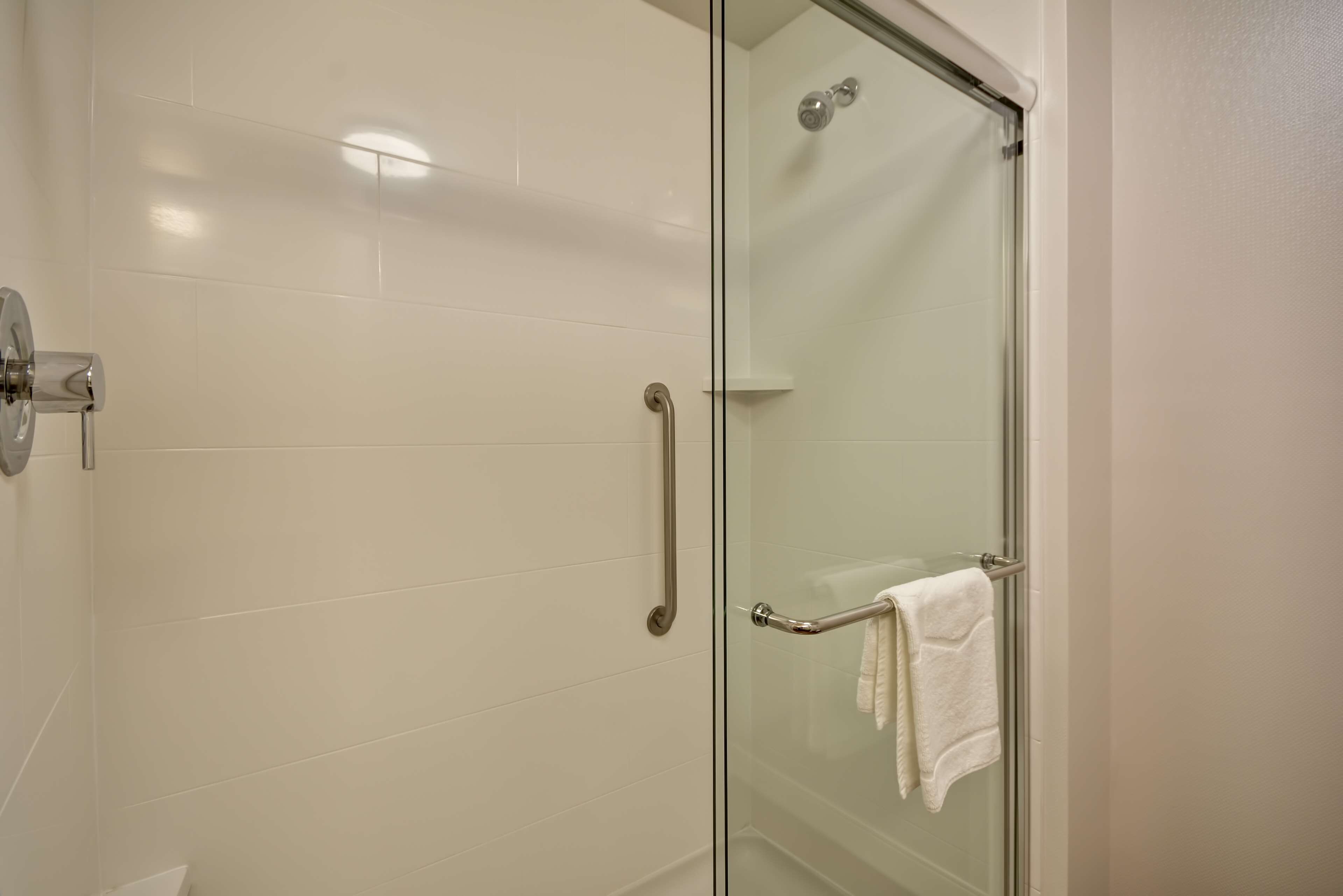 A glass-enclosed shower with a handrail and a towel rack.