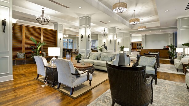 A spacious lobby with a sofa, chairs, and a coffee table, featuring a wooden floor and decorative lighting. - Hampton Inn & Suites Charleston Airport (North Charleston)