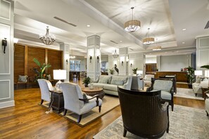 A spacious lobby with a sofa, chairs, and a coffee table, featuring a wooden floor and decorative lighting. - Hampton Inn & Suites Charleston Airport (North Charleston)
