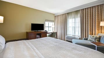 A hotel room with a large bed, a desk with a television, a chair, and a sofa.
