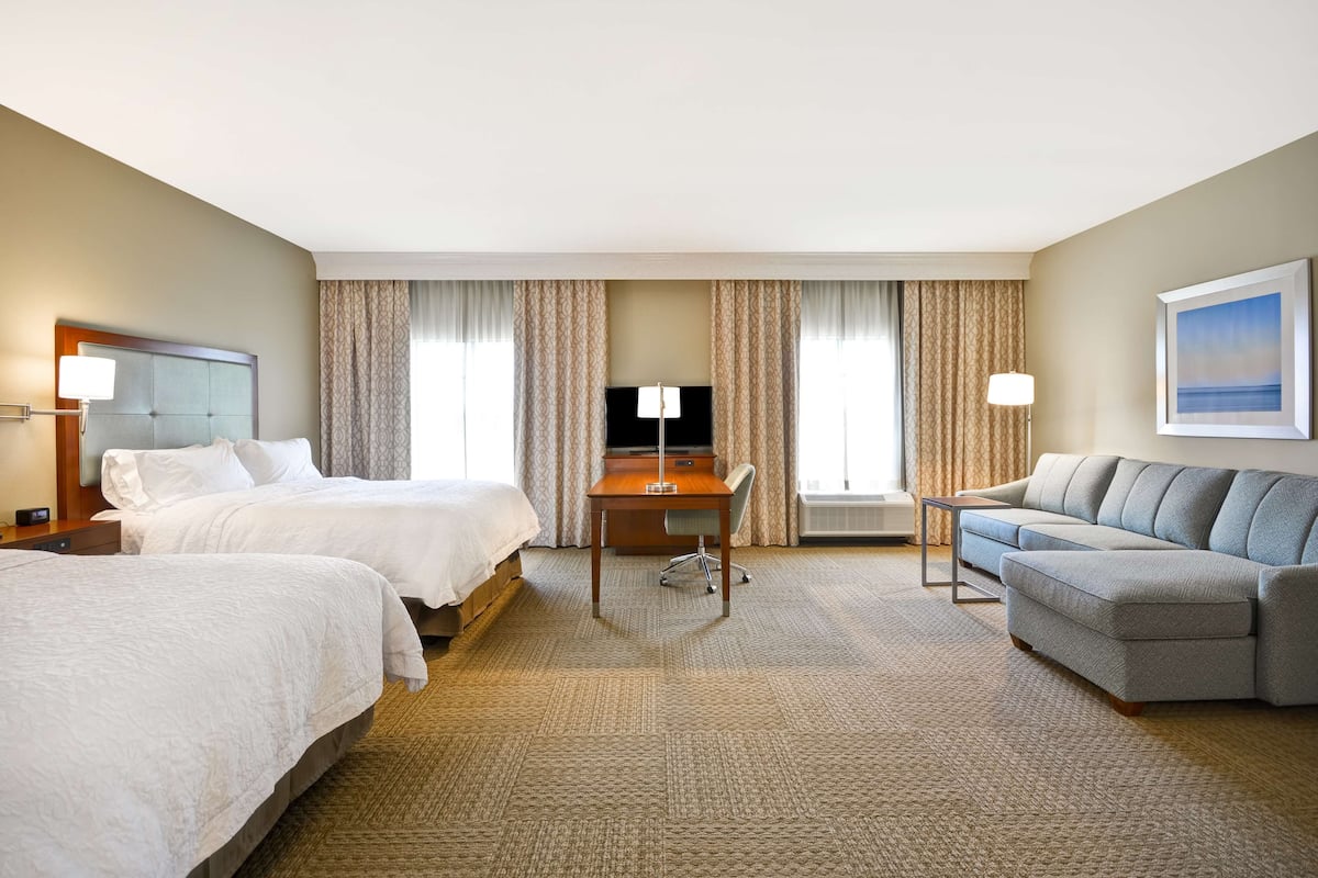 A hotel room with two beds, a desk, a sofa, and a TV.