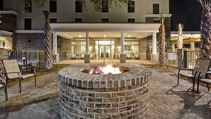 A courtyard with a fire pit, outdoor seating, and a building entrance in the background. - Hampton Inn & Suites Charleston Airport (North Charleston)