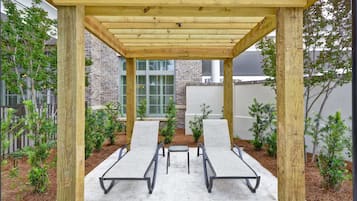 Ein überdachter Patio-Bereich mit zwei Liegestühlen und einem kleinen Tisch, umgeben von einer Backsteinmauer und Grünpflanzen.