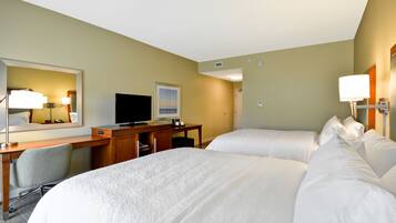 Habitación de hotel con dos camas, un escritorio, un televisor y un espejo grande.