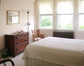 A bedroom with a large bed, a wooden dresser, a chair, and a radiator.