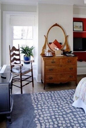 A bedroom with a wooden dresser, a chair with a plant, a patterned rug, and a television in the corner.