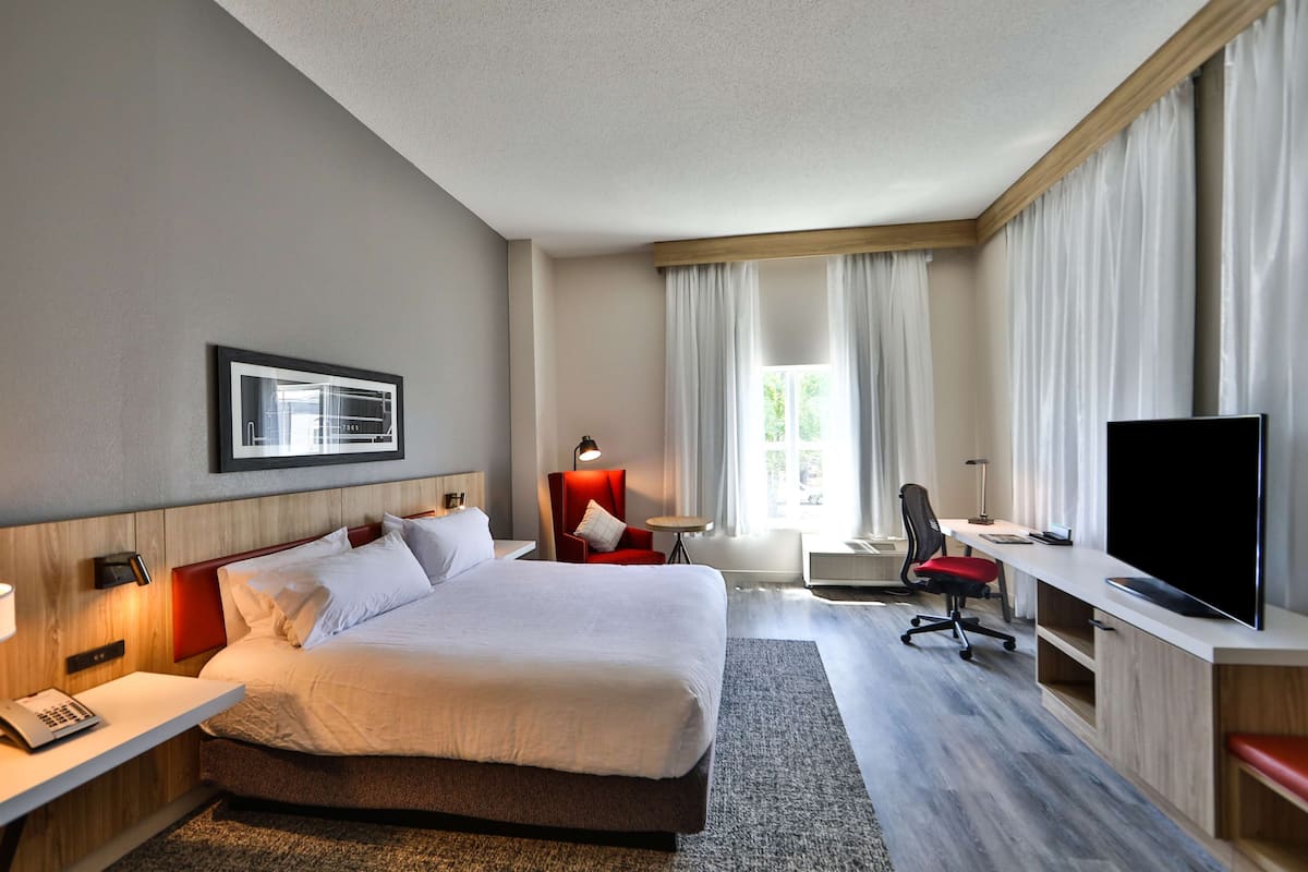 A hotel room with a large bed, a desk with a chair, a television, and a window with curtains.
