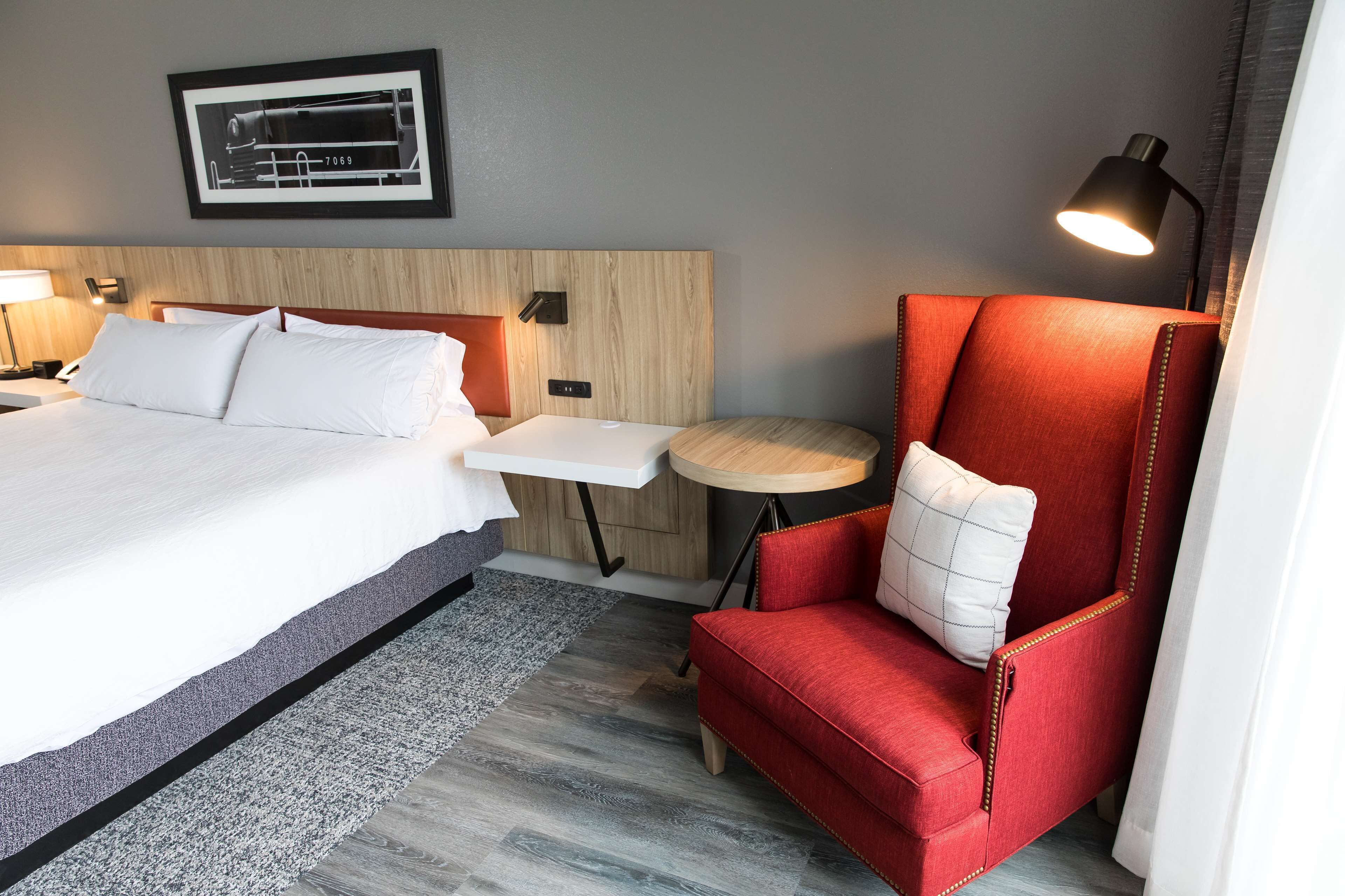 Ein Hotelzimmer mit einem großen Bett, einem roten Sessel, einem kleinen runden Tisch und einer Wandlampe.