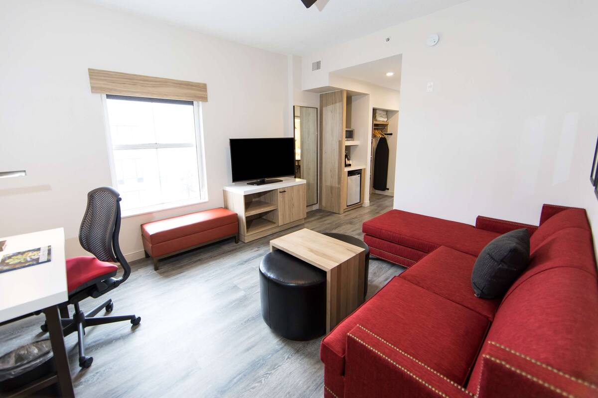 A modern living room with a red sofa, a black office chair, a wooden coffee table, and a flat-screen TV on a white stand.