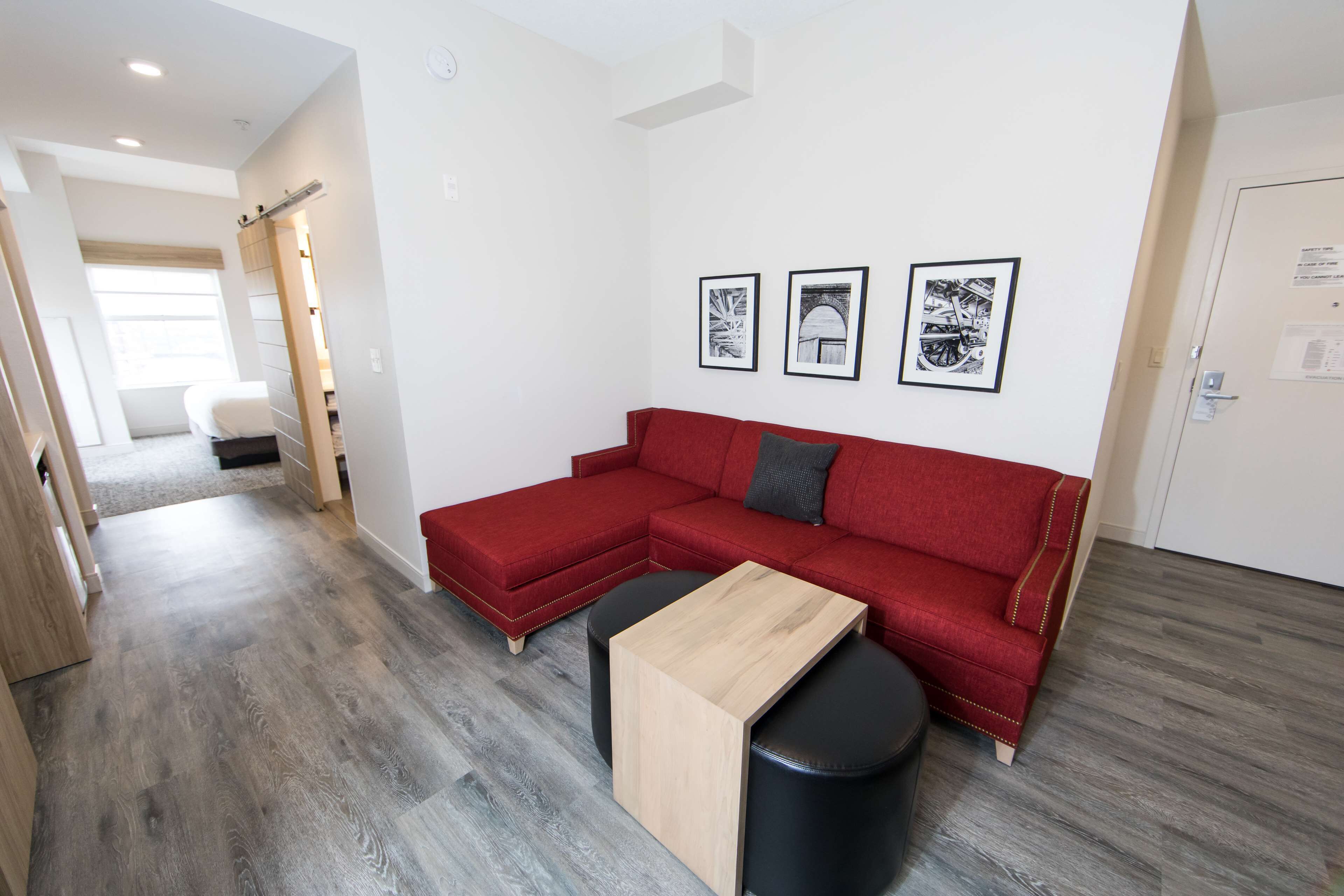 A modern living room with a red sectional sofa, a wooden coffee table, and black ottomans. There are three framed pictures on the wall.