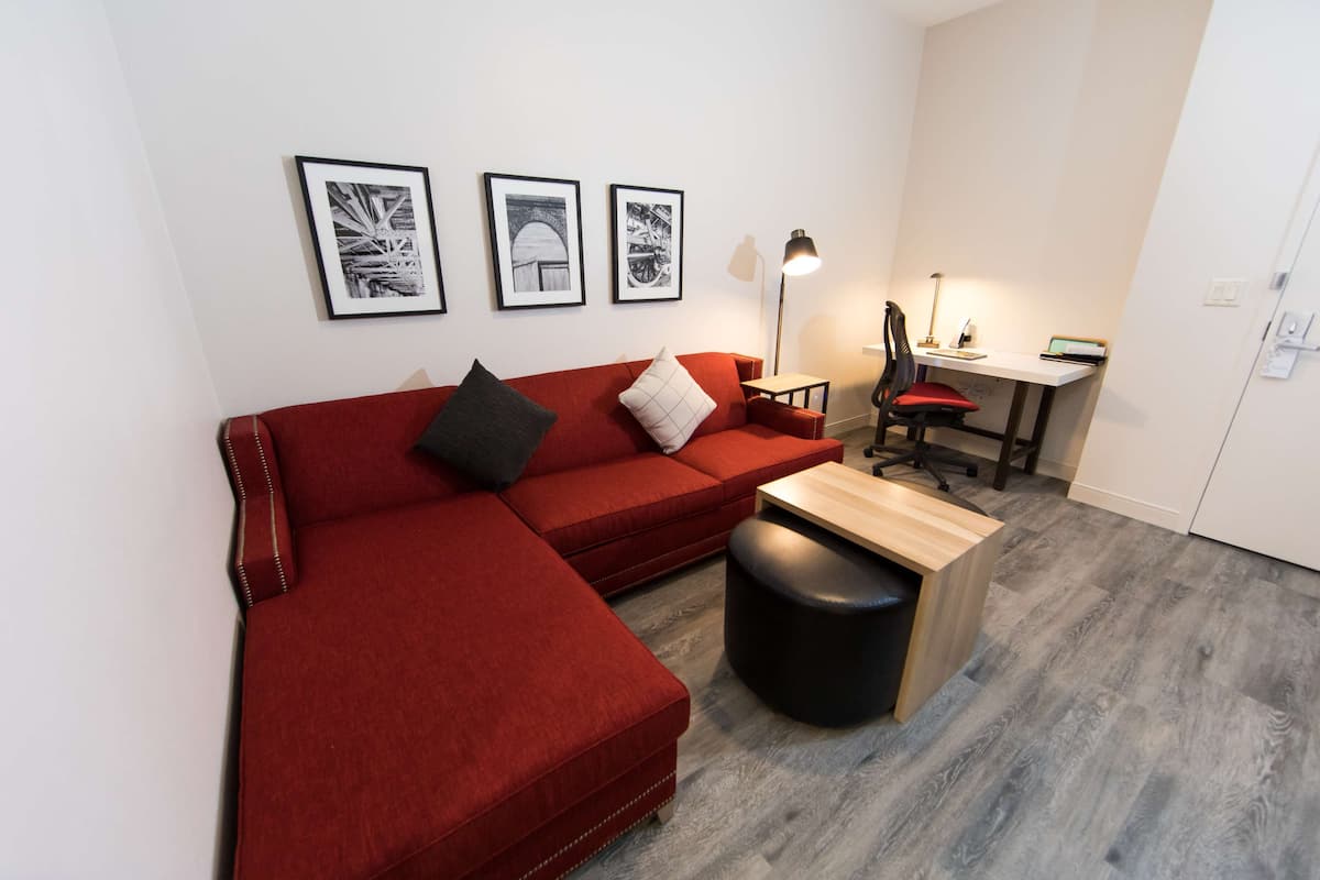 A modern living room with a red sectional sofa, a small wooden table, and a desk with a chair. There are three framed pictures on the wall.