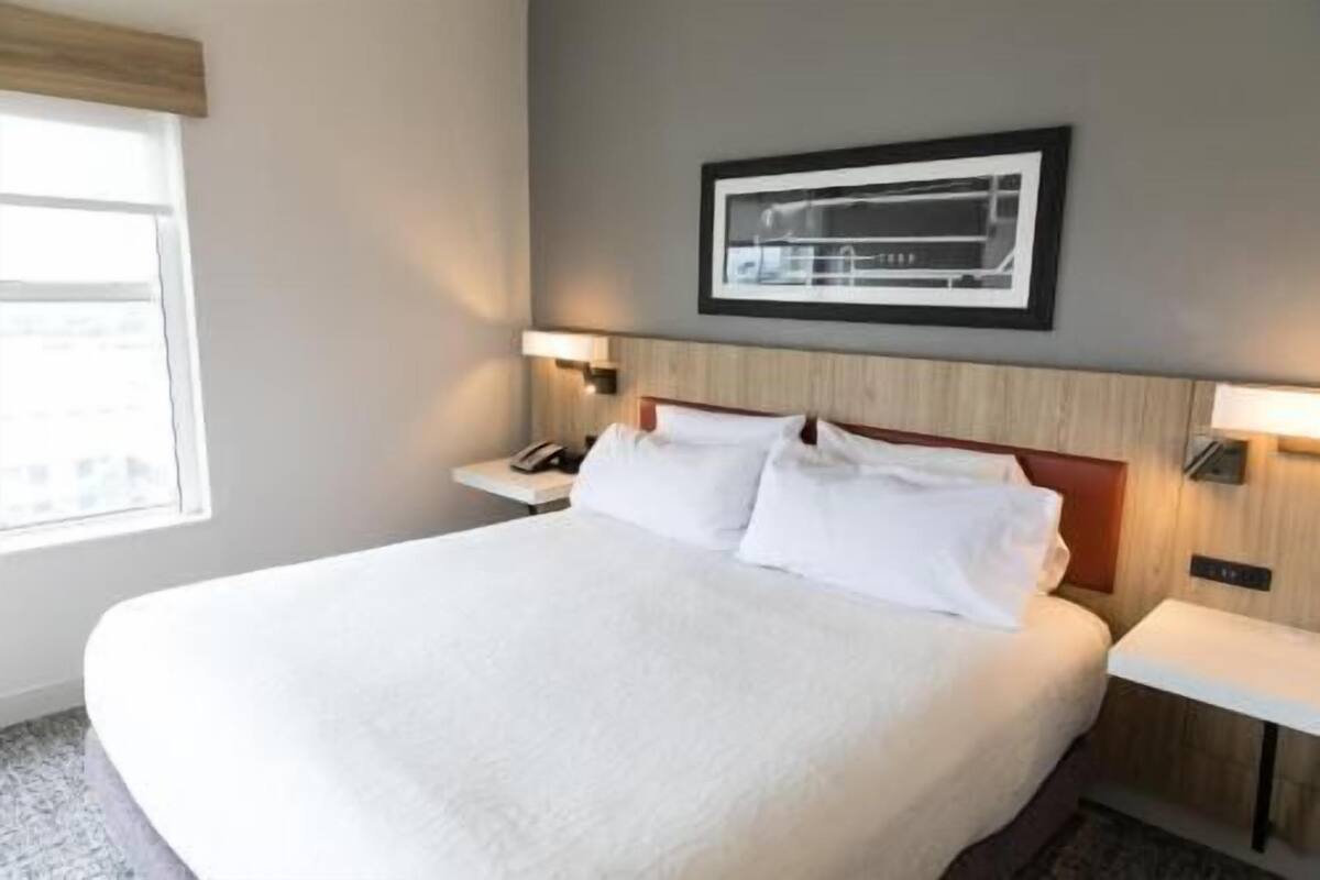 A hotel room with a large bed, bedside tables, a framed picture on the wall, and a window.
