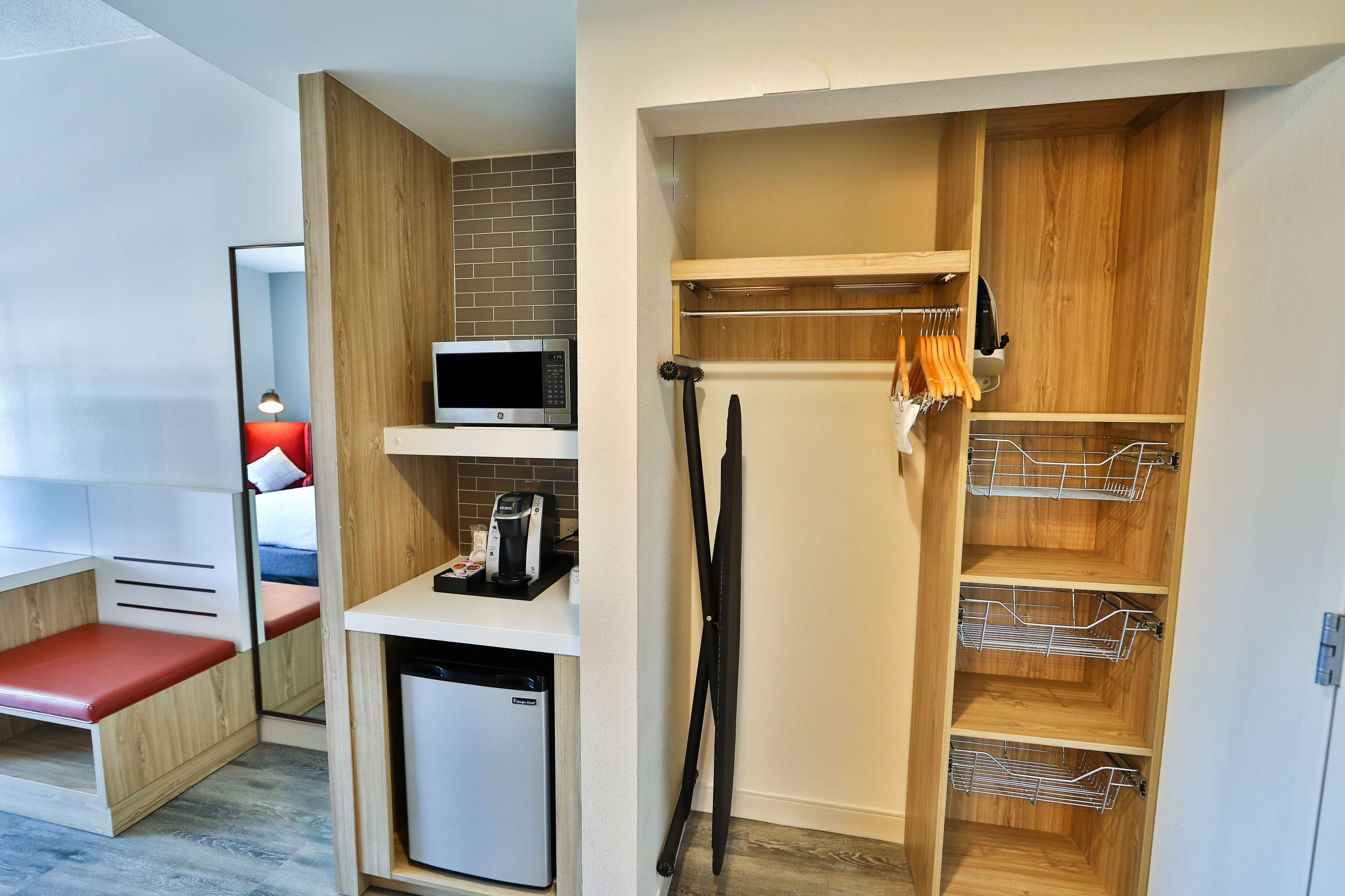 A compact room with a kitchenette, a microwave, a coffee maker, a small refrigerator, and a wooden wardrobe with shelves.