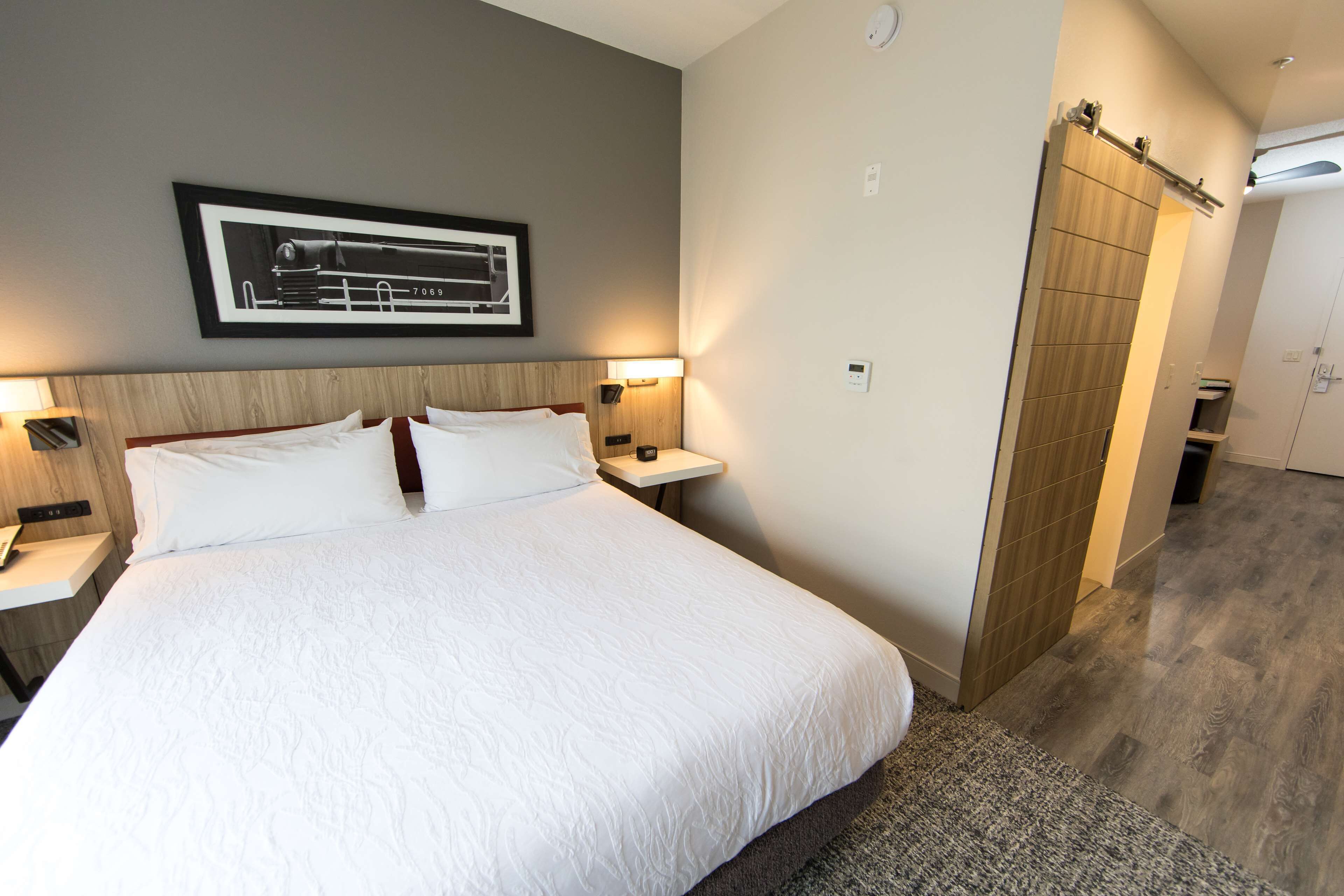 Une chambre d’hôtel avec un grand lit, deux tables de chevet avec des lampes, un tableau encadré au mur et une armoire.