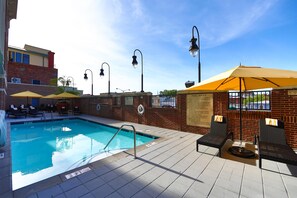 A swimming pool with lounge chairs and umbrellas, a brick wall, and a clear sky.