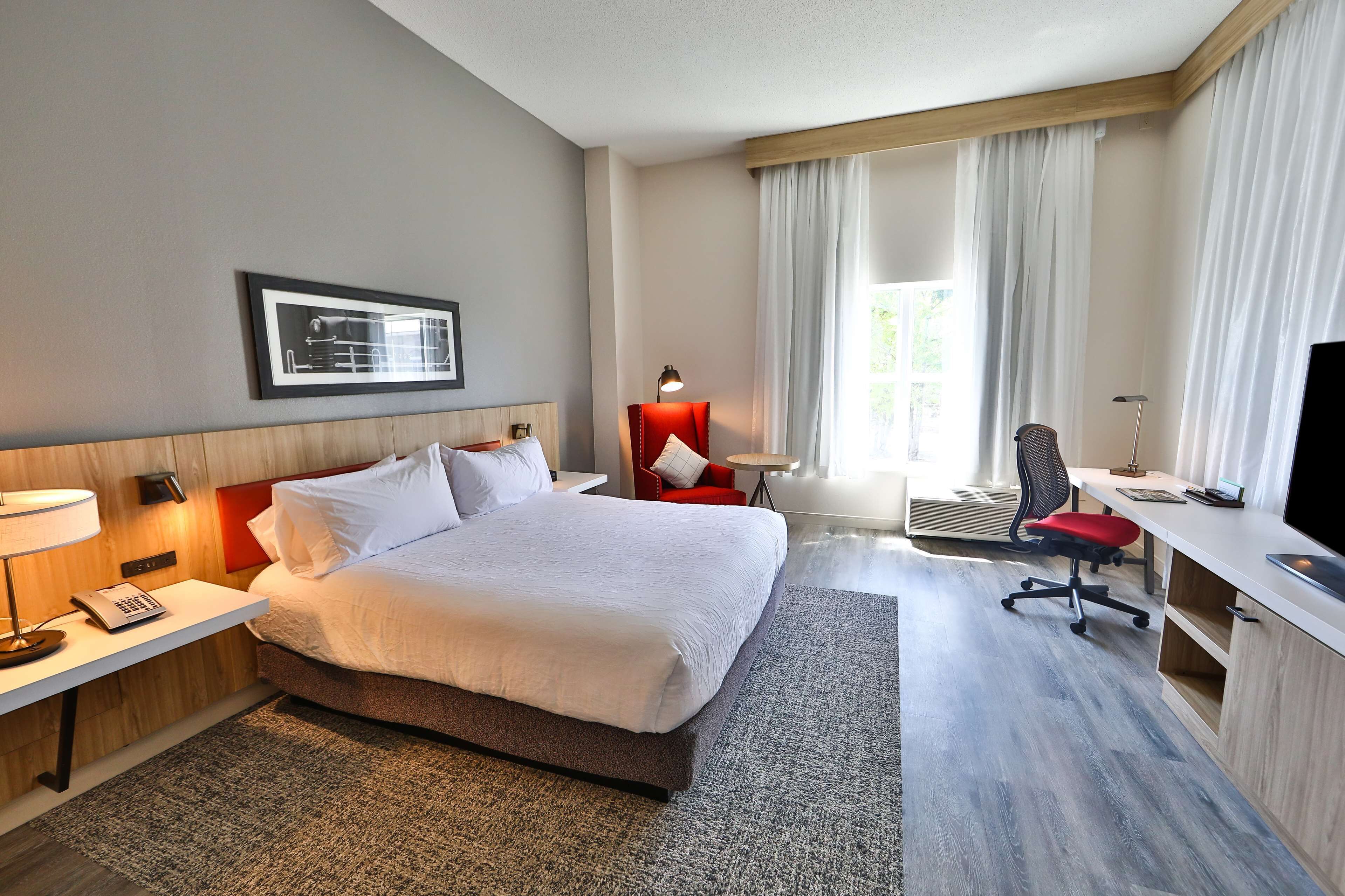 A hotel room with a large bed, a desk with a chair, a TV, and a window with curtains.