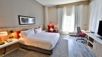 A hotel room with a large bed, a desk with a chair, a TV, and a window with curtains.