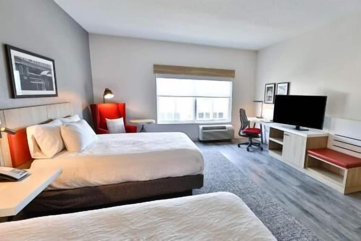A hotel room with two beds, a desk with a TV, a chair, and a window.