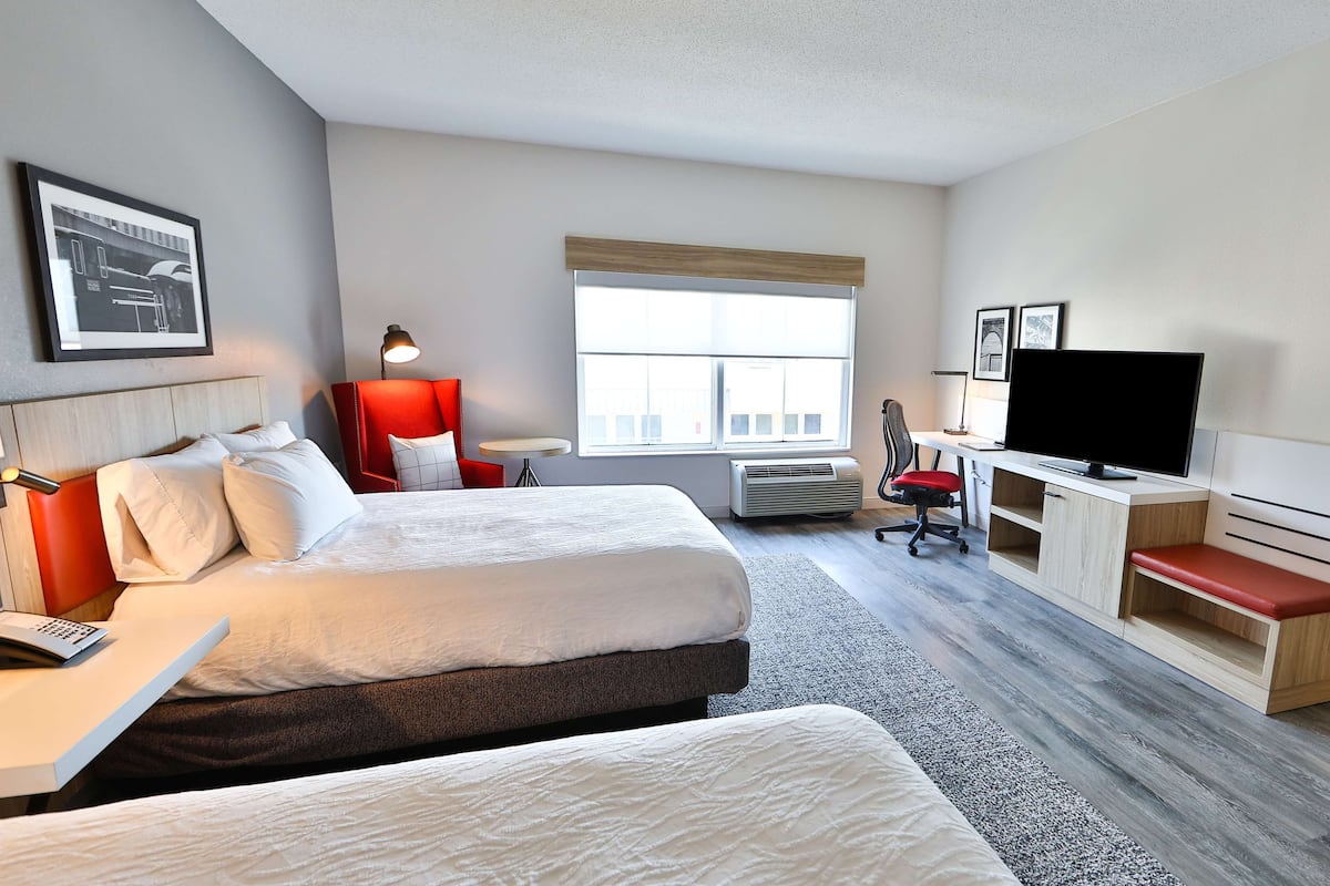 A hotel room with two beds, a desk, a television, and a window with a view.