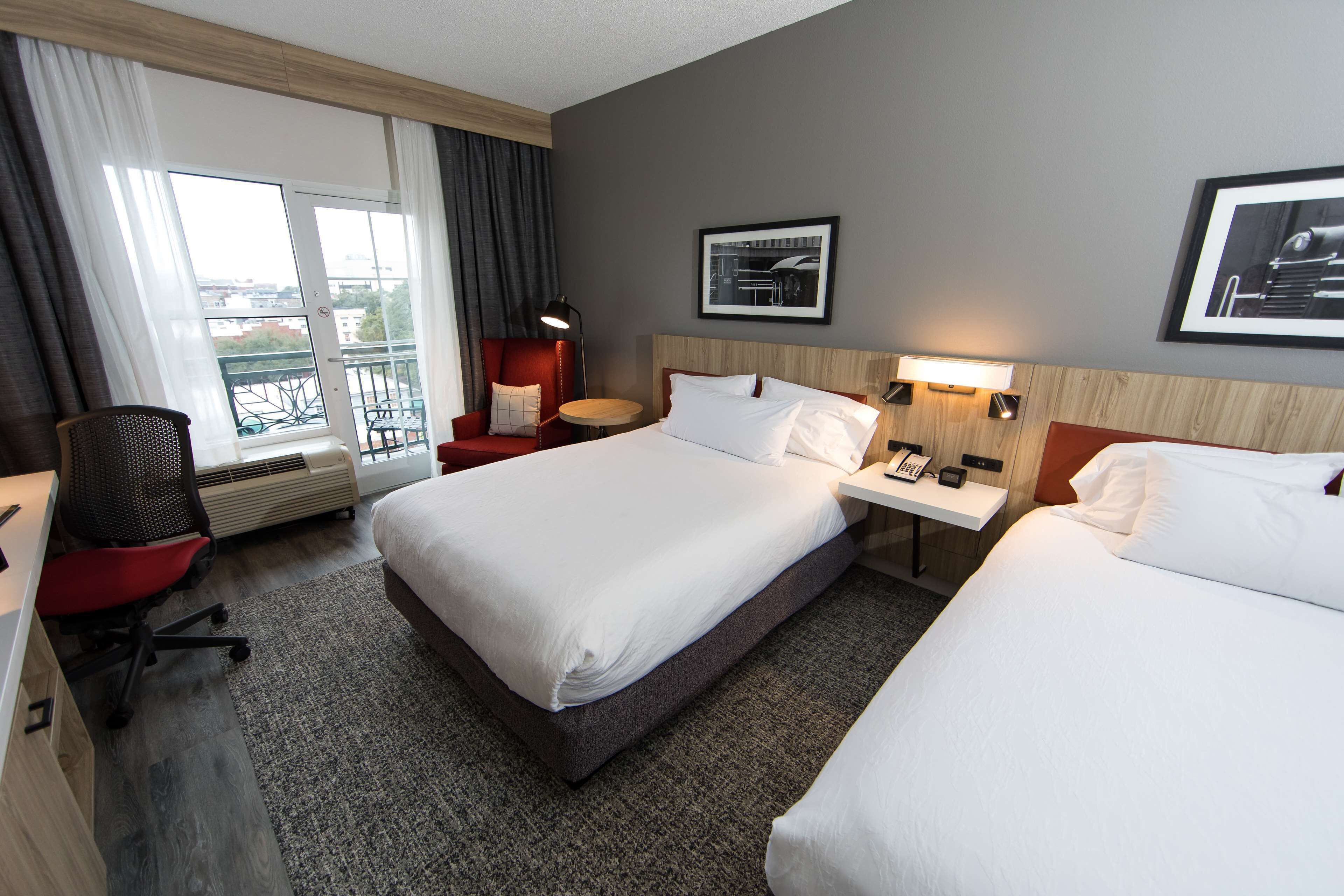 A hotel room with two beds, a desk, a chair, a small table, and a window with curtains.