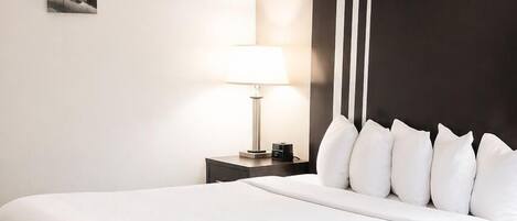 Una habitación de hotel con una cama grande, una mesita de noche con lámpara y una silla.